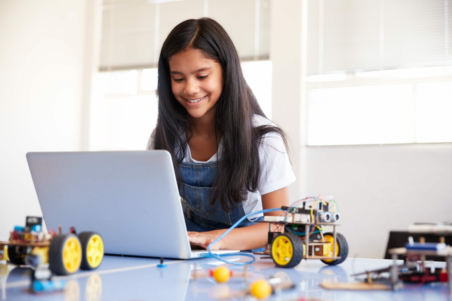 Image of a young girl looking at a computer with robotics equipment around her.