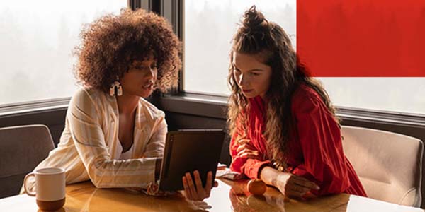 Two african american women sitting down looking at a tablet.