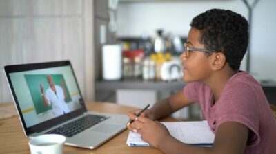 Image of an African American boy sitting at a computer doing an online lesson.